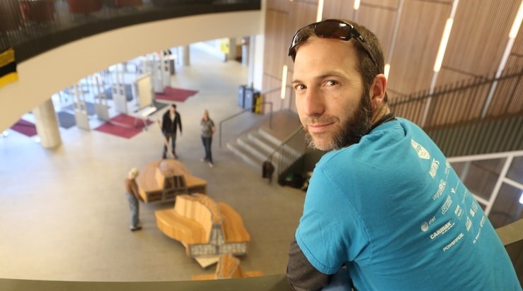 A portrait of the wood artist who created, designed and built the Fall Line bench for the library lobby. He is standing on the second floor that overlooks the lobby and the bench on the day it was assembled, March 3, 2018. Jay Paul photo.