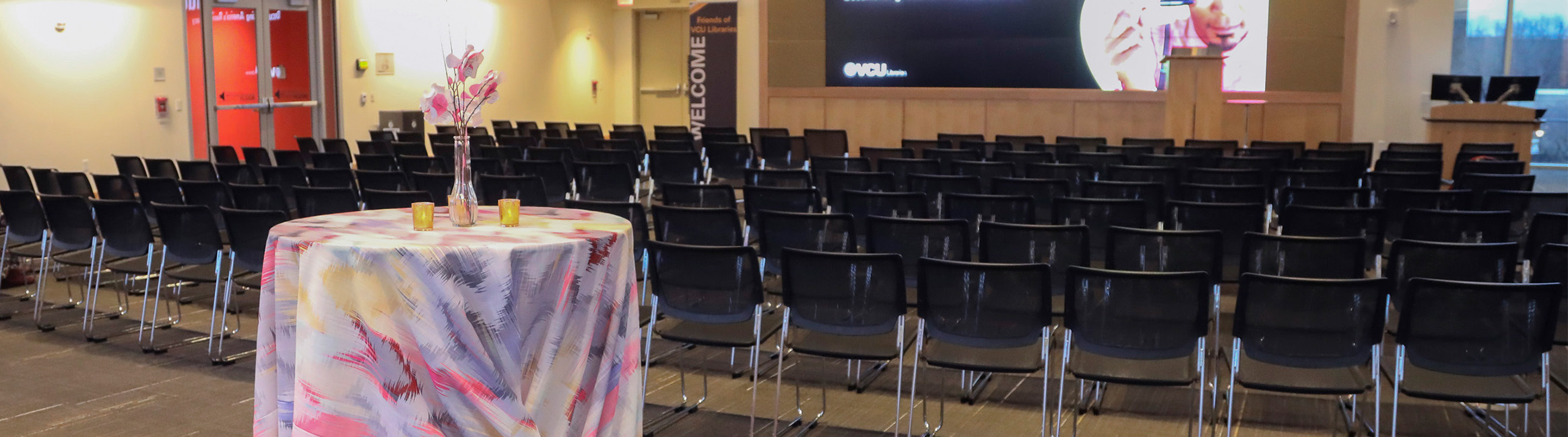 The Lecture Hall set up with chairs and a table with a table cloth and center piece.